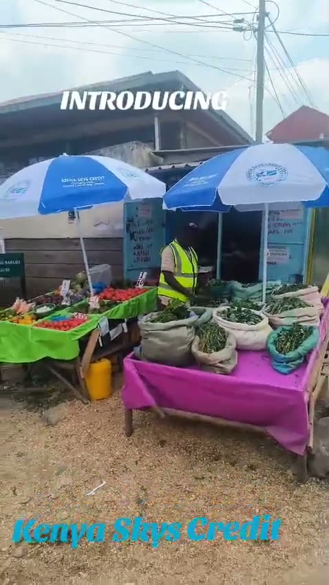A Kenya Skys Credit branded stall with two blue umbrellas at a roadside produce market